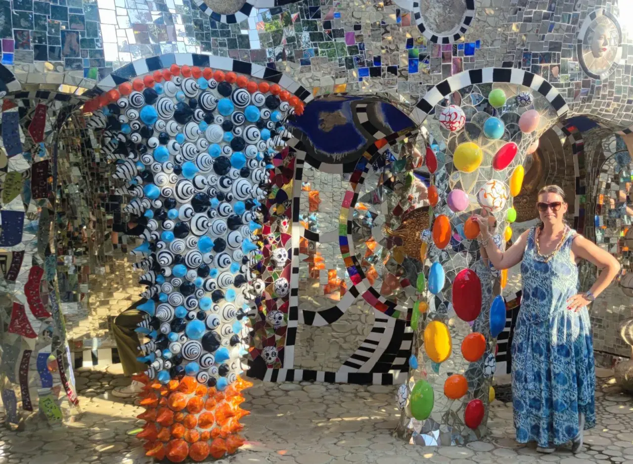 Donna sorride nel Giardino dei Tarocchi, un luogo magico pieno di mosaici colorati e sculture bizzarre.