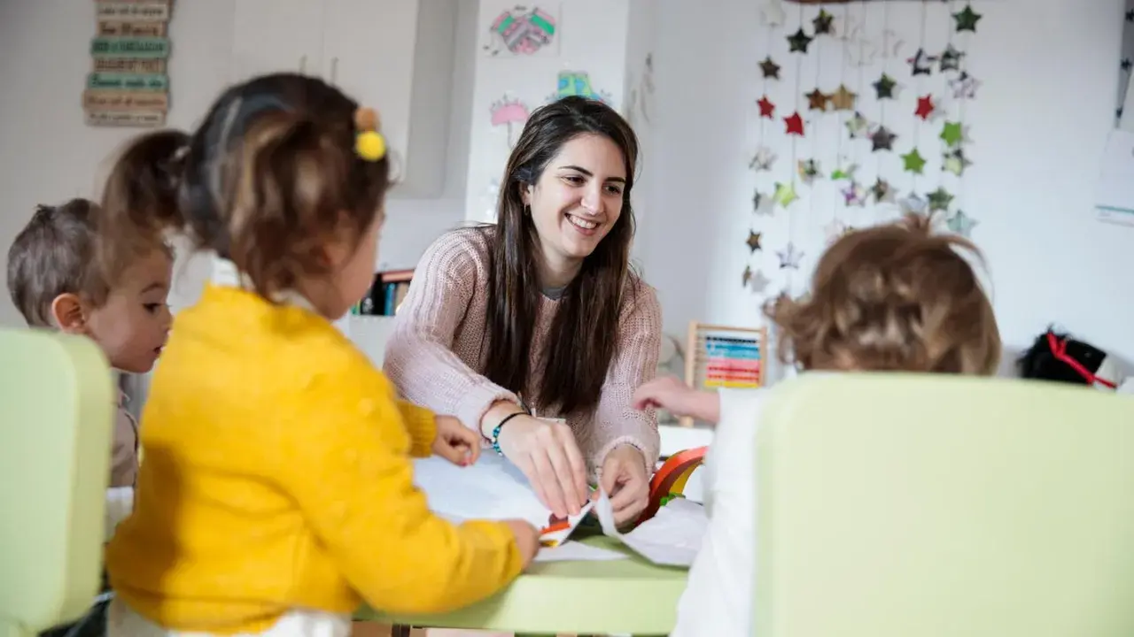 Eine Kinderpflegerin lächelt, während sie mit Kindern bastelt. Sie fragt sich, wie viel verdient man als Kinderpflegerin?