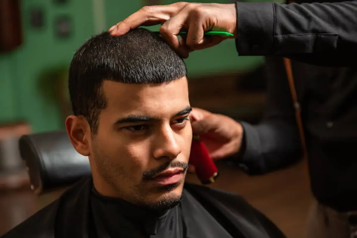 Mann bekommt einen Buzz Cut 15mm. Der Friseur trimmt das Haar mit einer Schere und einem Trimmer.