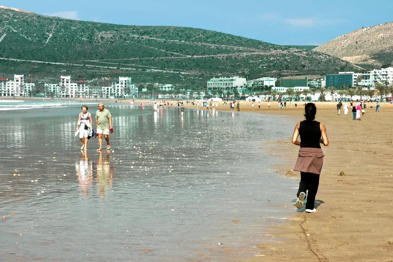 Spacerem po plaży w Maroku, w tle białe budynki i zielone wzgórza. Idealne wakacje.