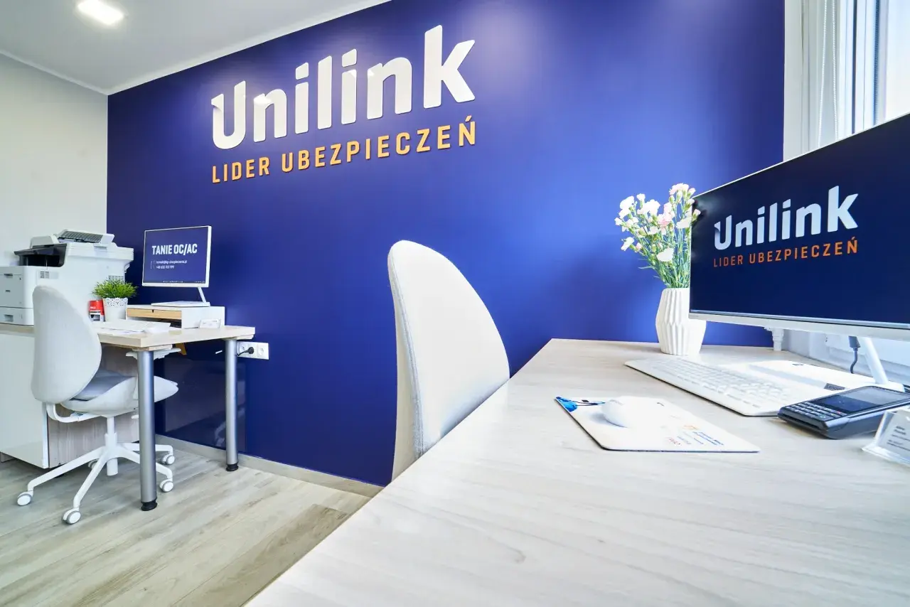 Biuro z niebieską ścianą z logo Unilink, biurkiem, komputerem i krzesłem.