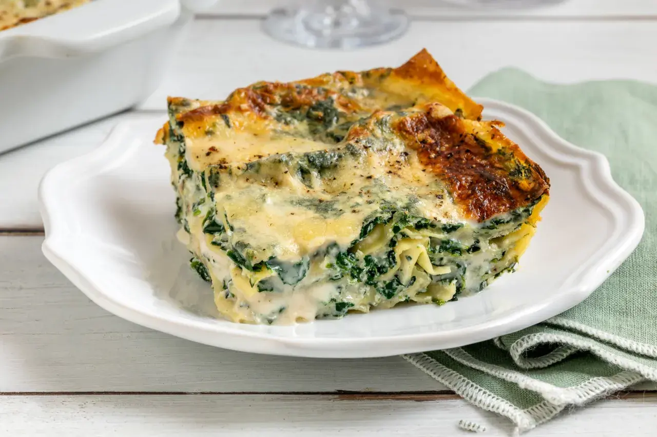 Una fetta di lasagne ricotta e spinaci, dorata al forno, su un piatto bianco.