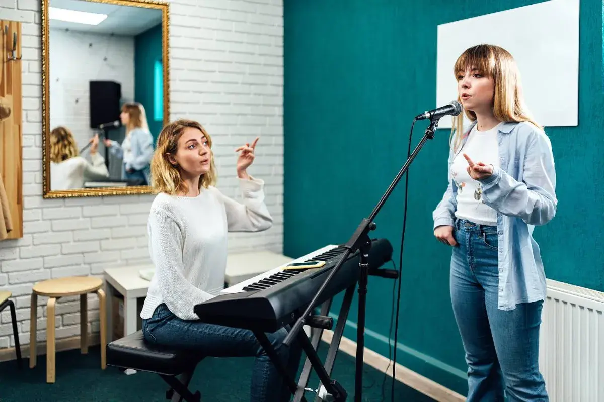 Lekcja śpiewu w domu: nauczycielka przy keyboardzie instruuje uczennicę przed mikrofonem.