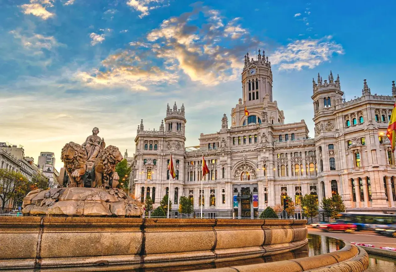 Cibelesfontänen framför det ståtliga Palacio de Comunicaciones, ett ikoniskt konstmuseum i Madrid, under en dramatisk solnedgång.