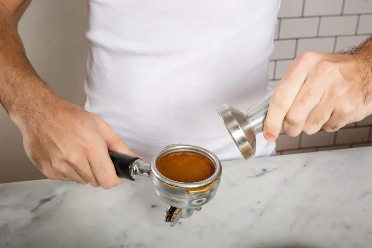 Ręce przygotowują kawę cappuccino, ubijając świeżo zmieloną kawę w portafiltrze.