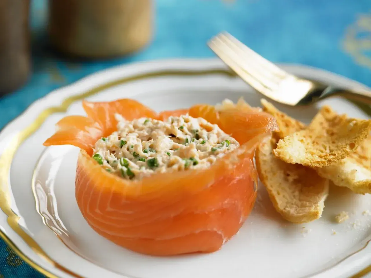 Ein appetitlicher **Salat mit Fisch**, serviert in einem Lachs-Cup, mit knusprigen Brotscheiben und einer goldenen Gabel.