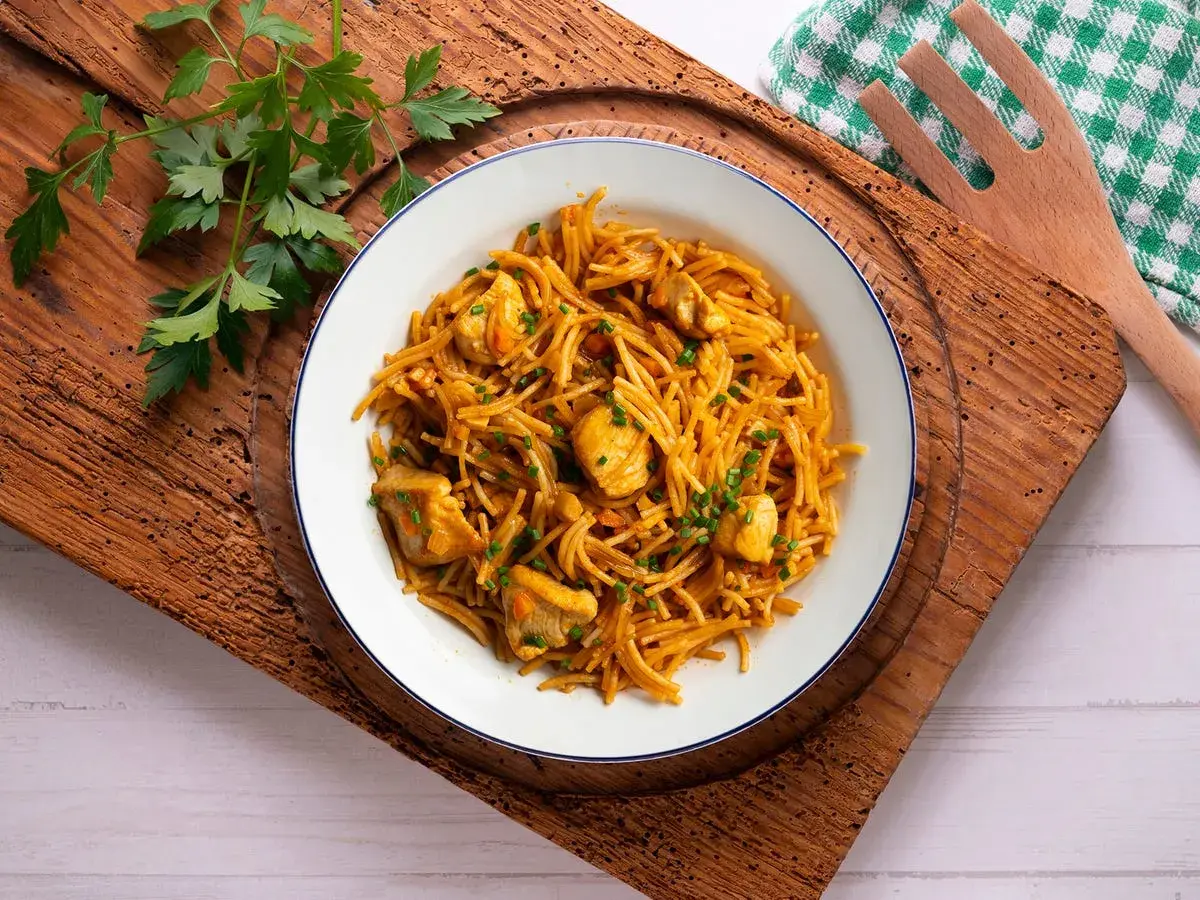 Delicioso plato de fideuà de pollo, con fideos finos y trozos de pollo tierno, decorado con perejil fresco.