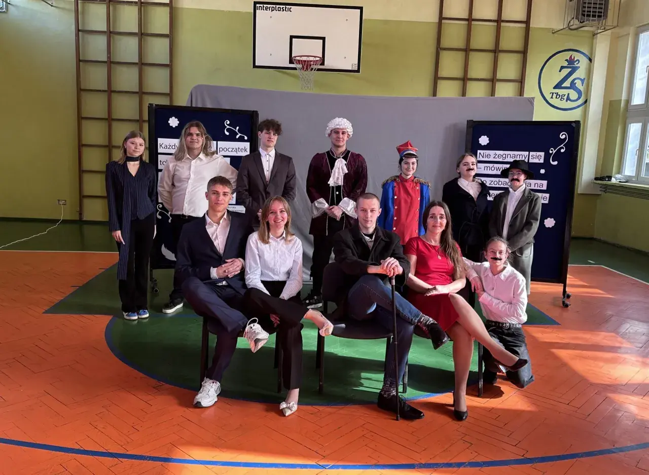 Uczniowie w strojach teatralnych, przygotowujący piosenkę absolwenta.