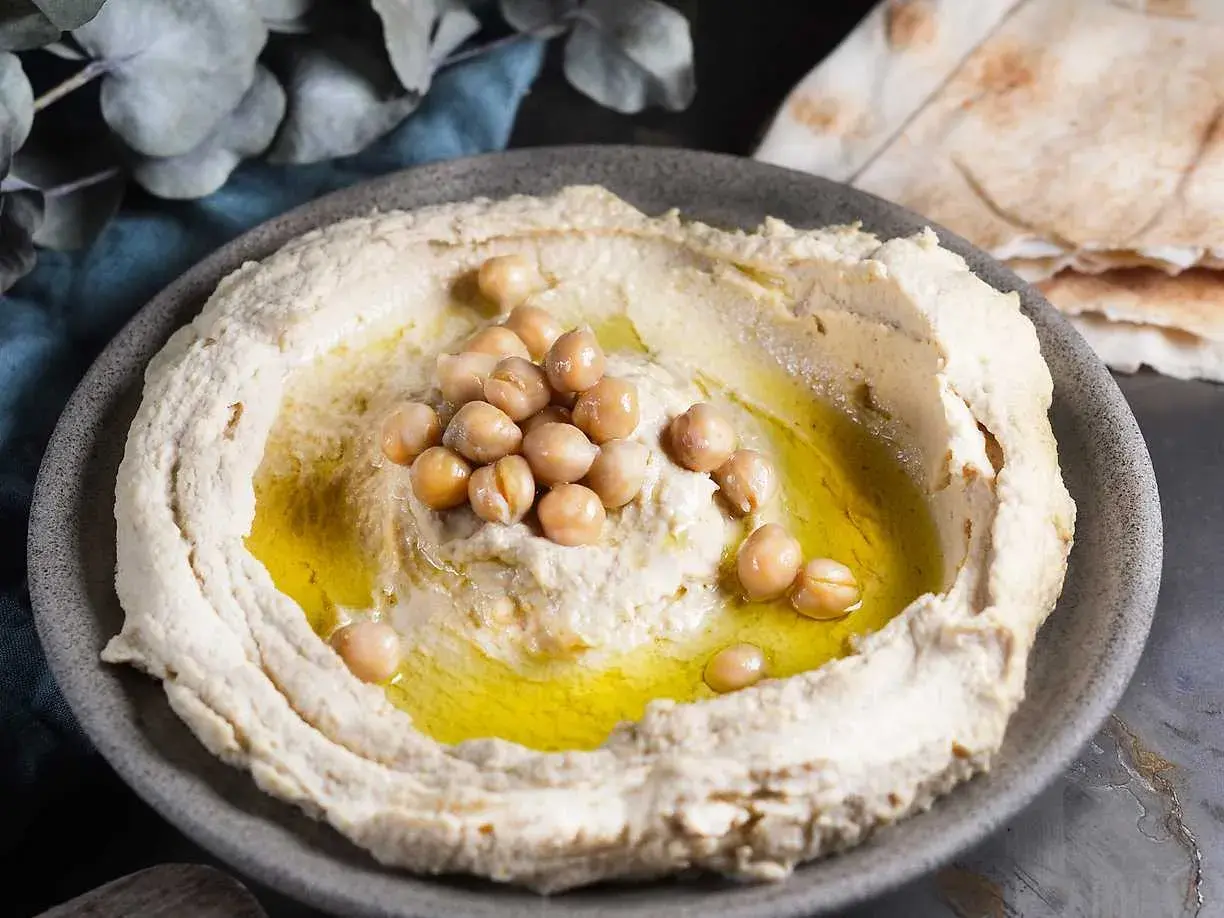 Krämig hummus med kikärtor och olivolja, perfekt för ett enkelt hummus recept. Serveras med pitabröd.