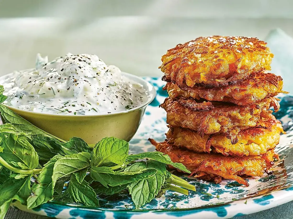 En stapel gyllene halloumi morotsbiffar serveras med en krämig yoghurtsås och färsk mynta.