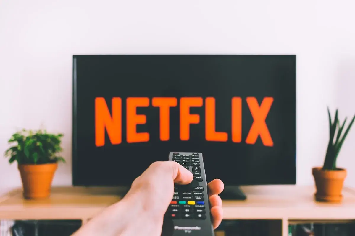 En hand håller en fjärrkontroll framför en TV med Netflix-loggan. Perfekt för bra filmtips ikväll!