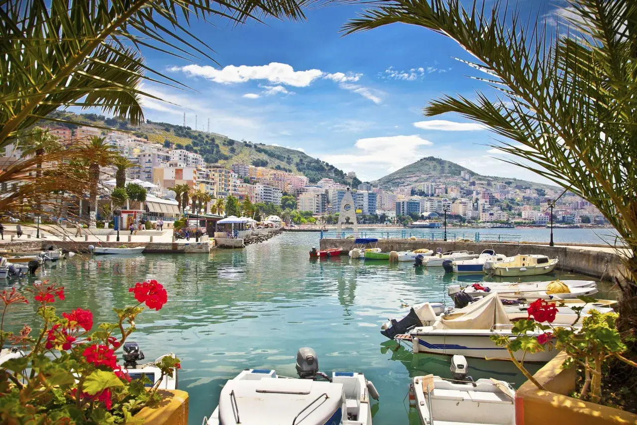 Albania - wczasy samolotem all inclusive. Widok na port z łodziami i kolorowymi budynkami na wzgórzu.