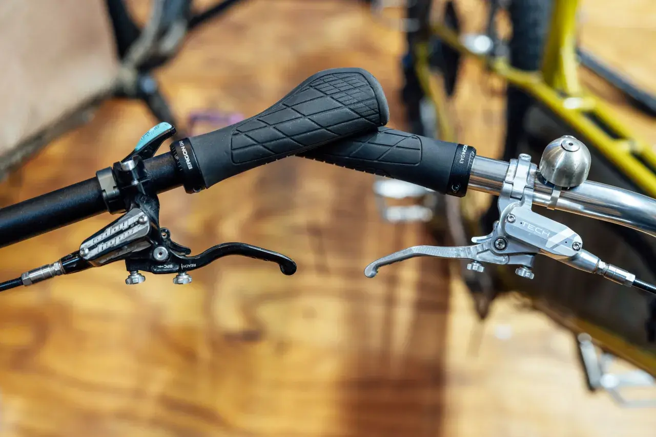 Close-up of bicycle handlebars featuring black Ergon grips and silver and black Hope e4 brakes, ready for any trail.