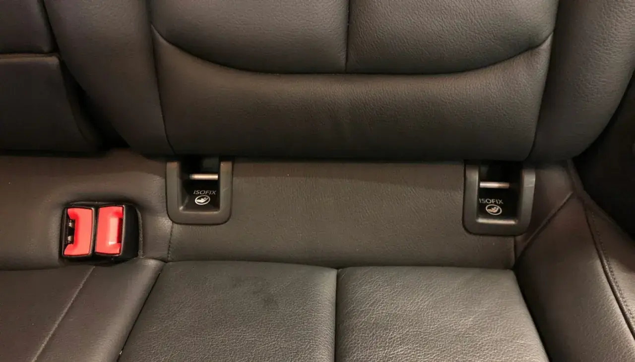 Widok na tylne siedzenia samochodu z widocznymi zaczepami **isofix jak wygląda** oraz czerwonymi klamrami pasów bezpieczeństwa.