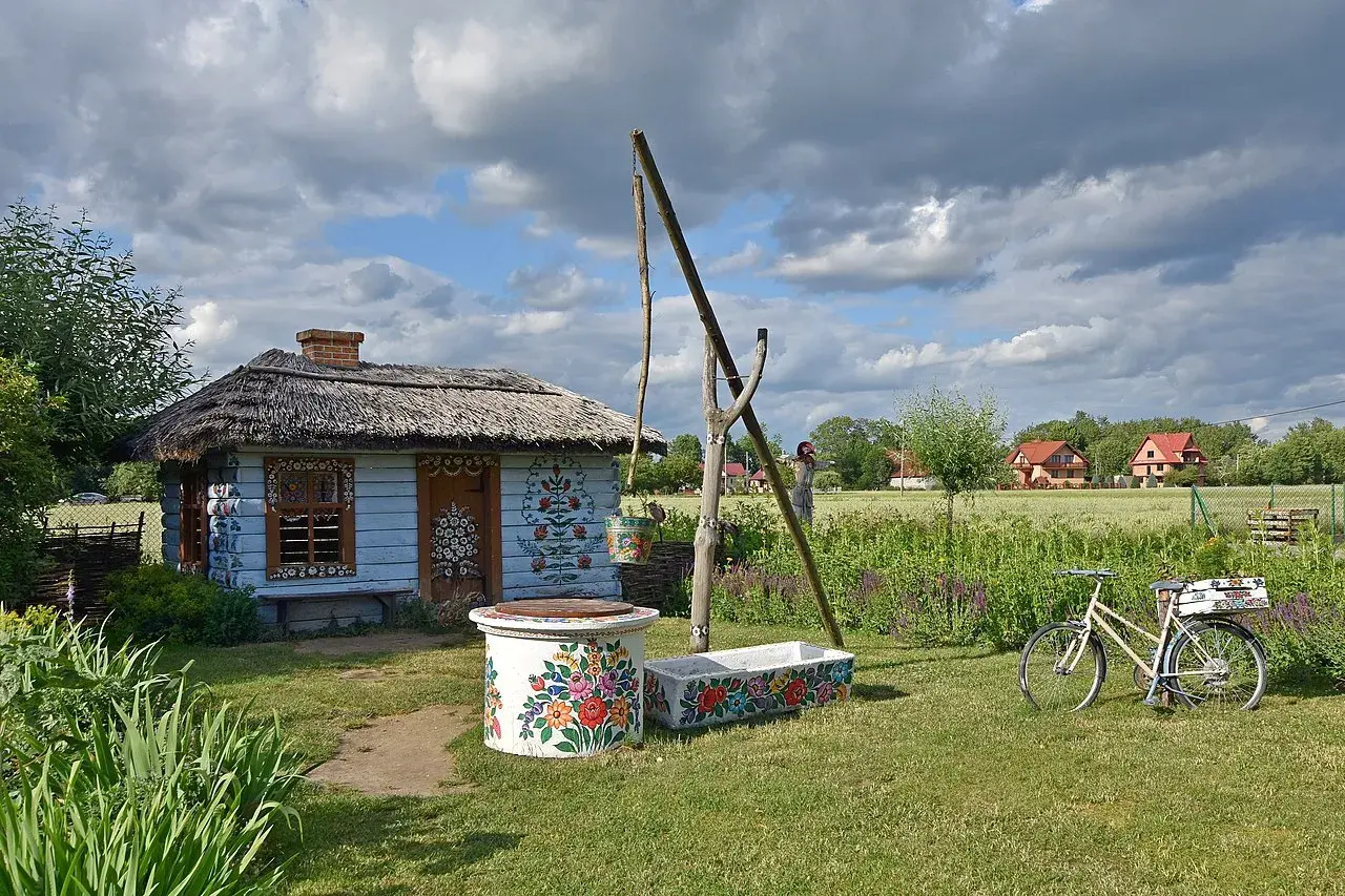 Kolorowy dom malarek w Zalipiu, z kwiecistymi zdobieniami, studnią i rowerem.