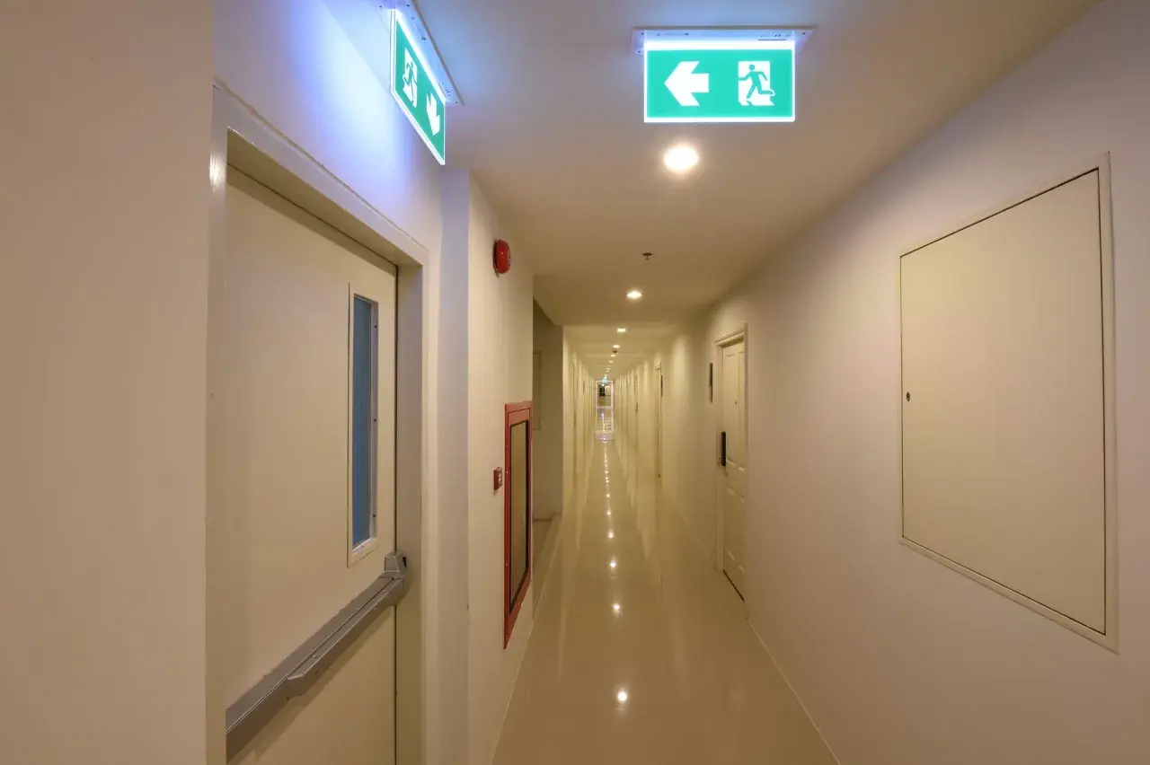 Korytarz hotelowy z zielonymi znakami ewakuacyjnymi, zgodnymi z normą PN-EN 1838.