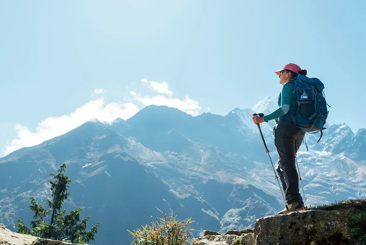 Kobieta z plecakiem i kijkami trekkingowymi podziwia majestatyczne góry. To jej wycieczka na Mount Everest, pełna wyzwań i piękna.