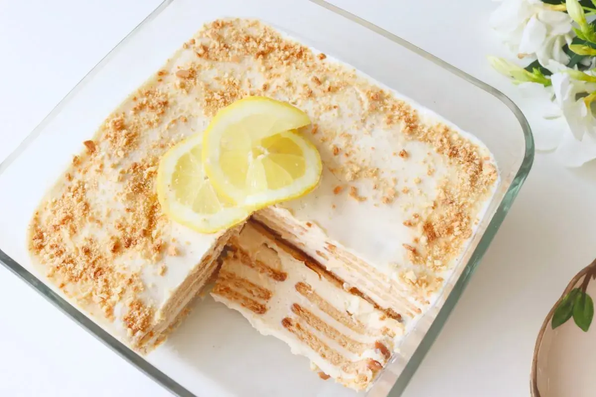 Deliciosa carlota de limón en un recipiente de vidrio, decorada con rodajas de limón y migas de galleta.