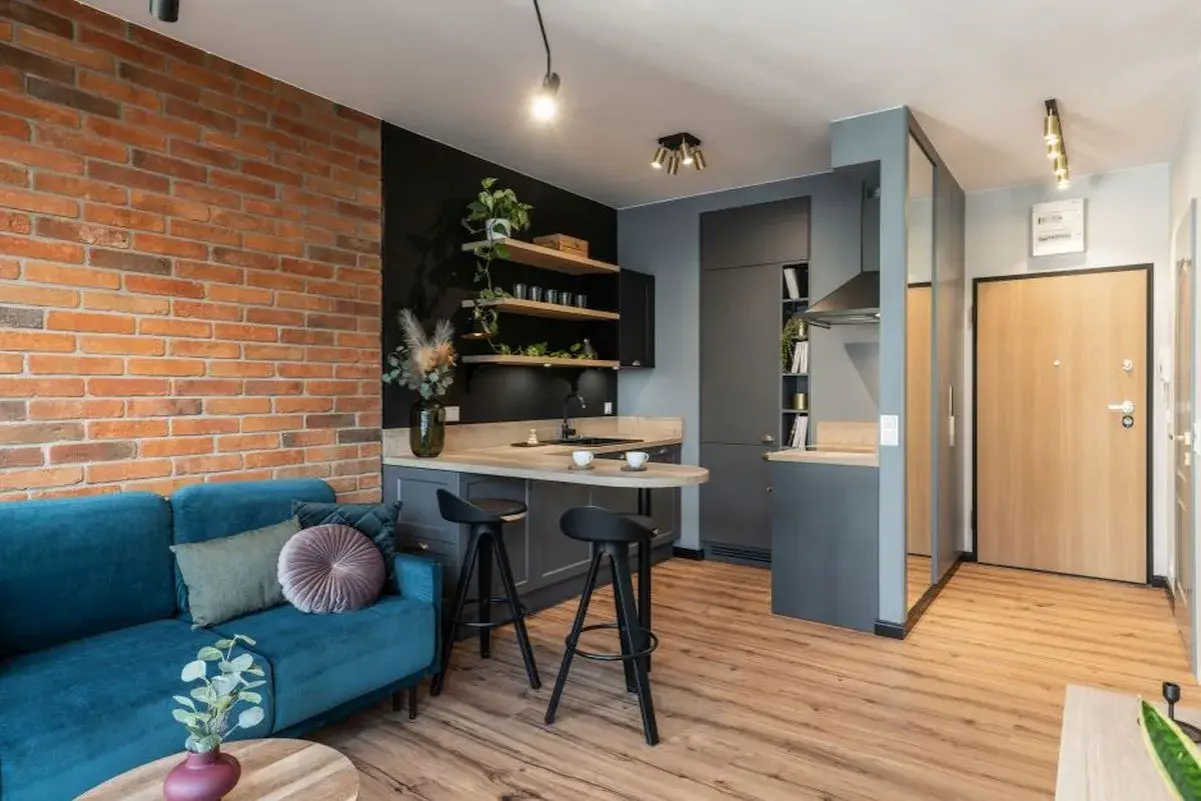 Nowoczesne mieszkanie 35m2 plan: salon z turkusową kanapą, kuchnia z wyspą i ceglaną ścianą.