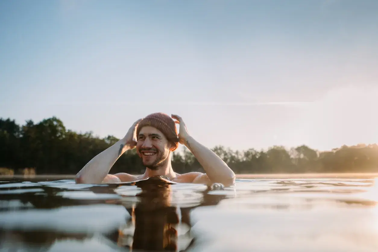 Uśmiechnięty mężczyzna w czapce zanurzony w wodzie, czuje się jak po zaawansowanym wim hof oddychanie poziom 2.