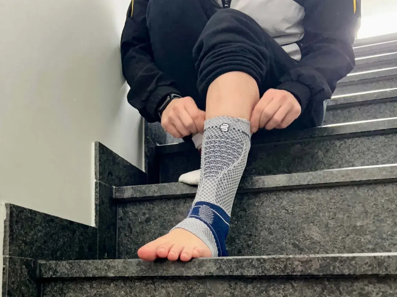 Person zieht eine Bandage am Fuß an, die bei einem Achillessehnenriss Schuh-Schmerzen helfen soll.