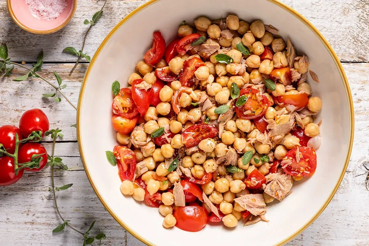 Un'insalata di ceci estiva con pomodorini freschi e tonno, guarnita con erbe aromatiche. Perfetta per un pasto leggero e gustoso.