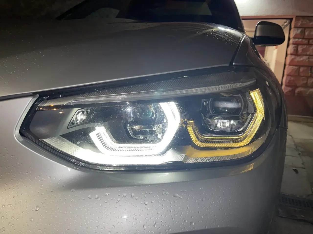 Gros plan sur un phare led qui clignote, illuminant la carrosserie mouillée d'une voiture argentée.
