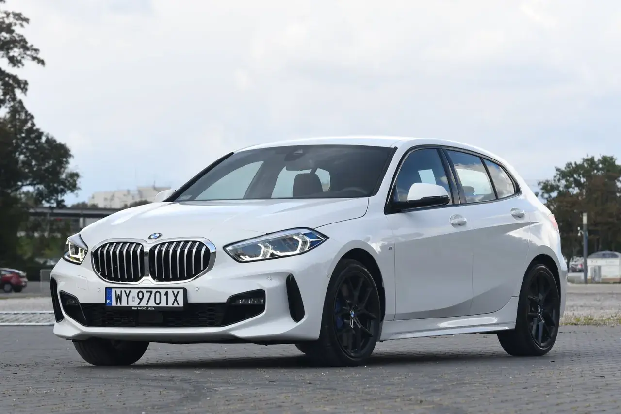 Białe BMW 118d z czarnymi felgami stoi na parkingu.