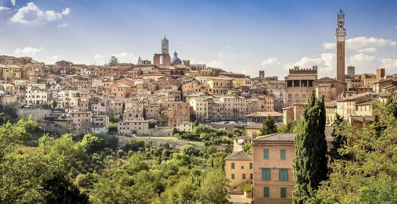 A panoramic view of Siena's historic skyline, a beautiful destination on the journey from Lucca to Siena. The Torre del Mangia tower stands tall amidst terracotta rooftops.