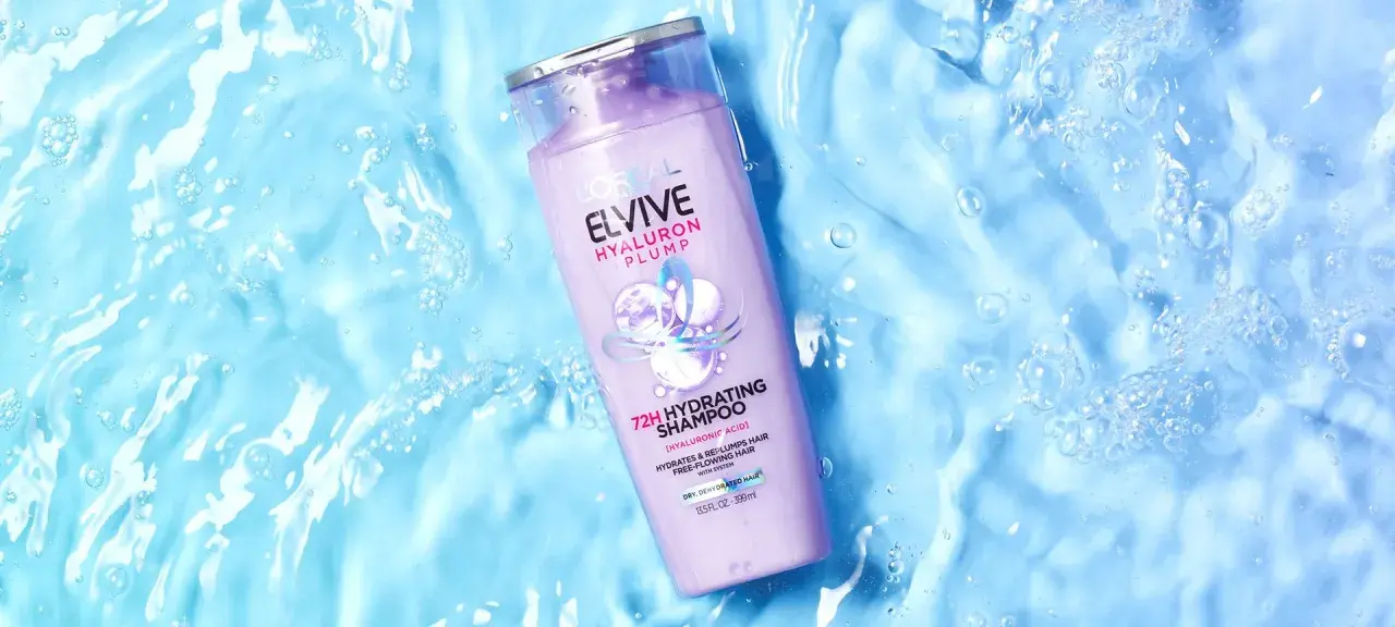 Botella de champú Elvive Hyaluron Plump sobre fondo azul con burbujas, ideal para pelo seco.