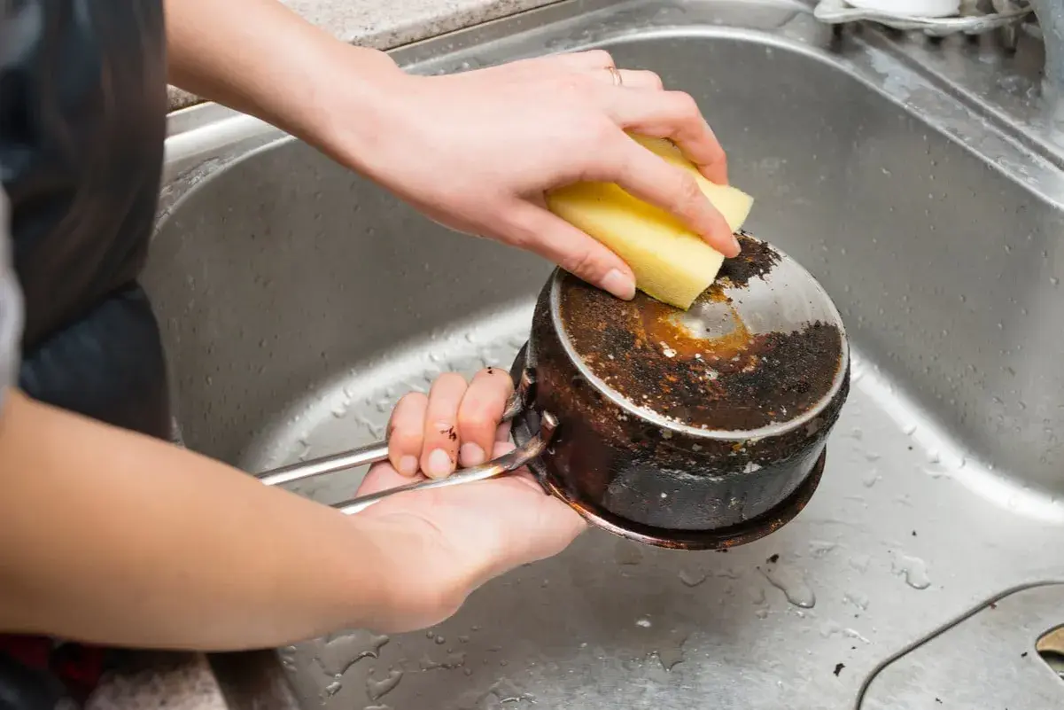 Nettoyage d'une casserole brûlée avec une éponge. Le bicarbonate de soude sera utile pour cette tâche difficile.