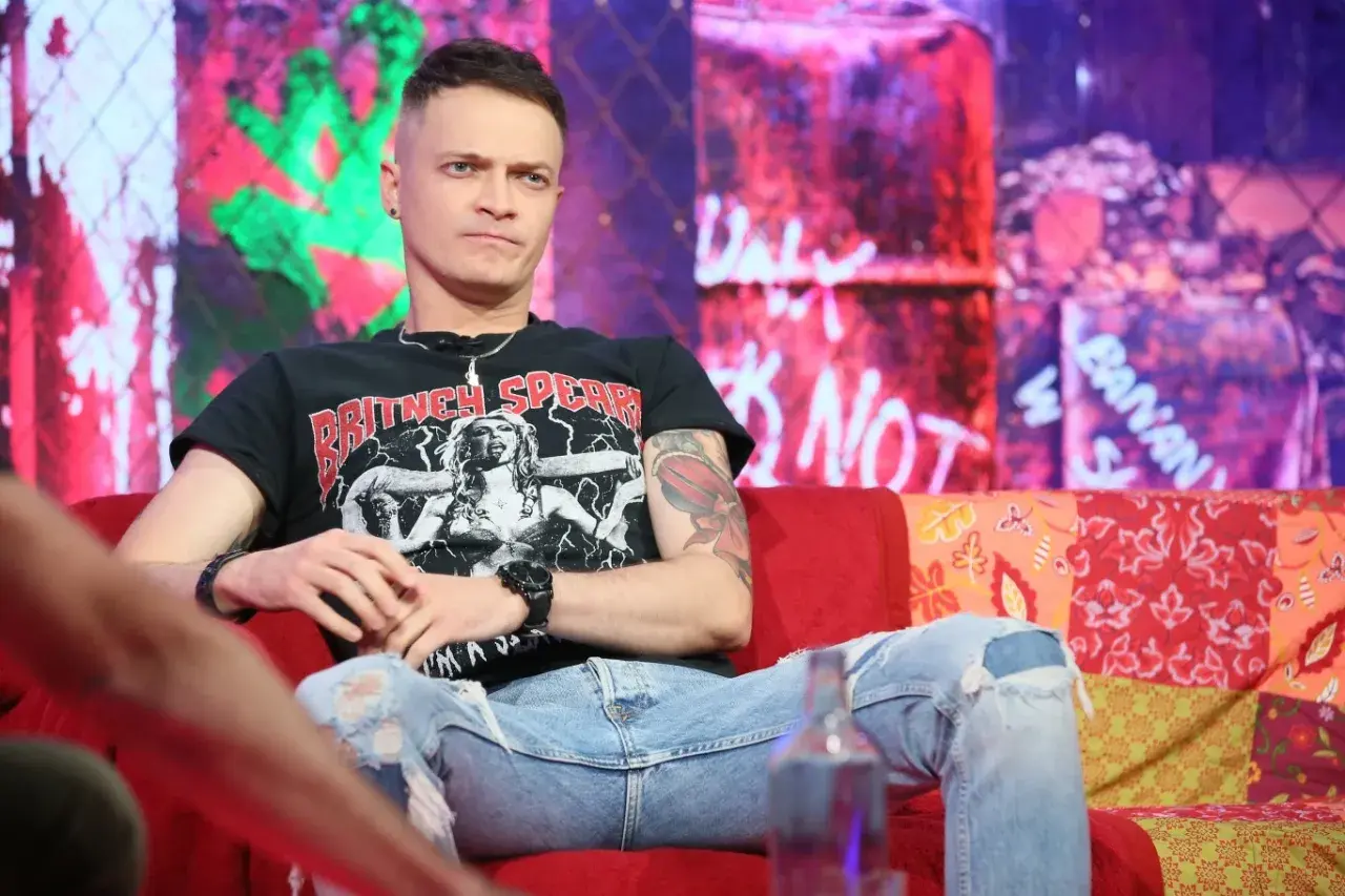 Nocny kochanek wokalista w czarnej koszulce z Britney Spears, siedzi na kanapie w podartych jeansach.