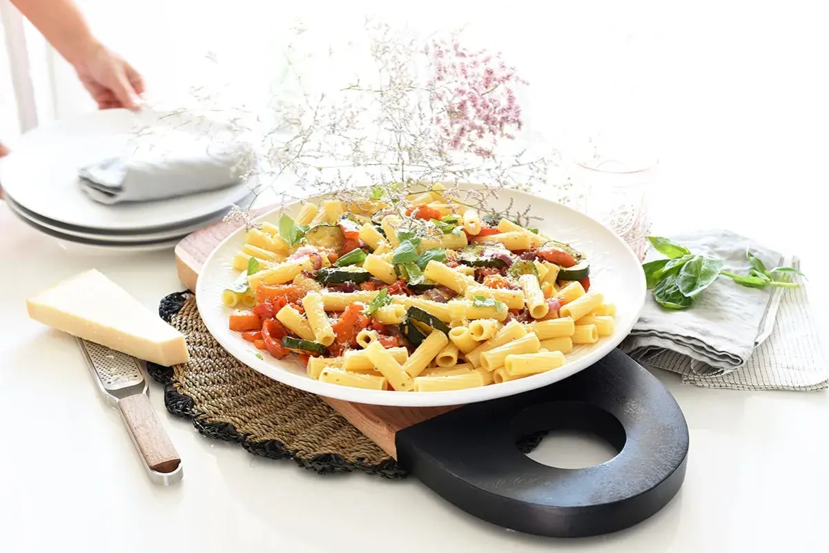 Plato de pasta con verduras salteadas, calabacín, tomate y albahaca, con queso parmesano rallado.