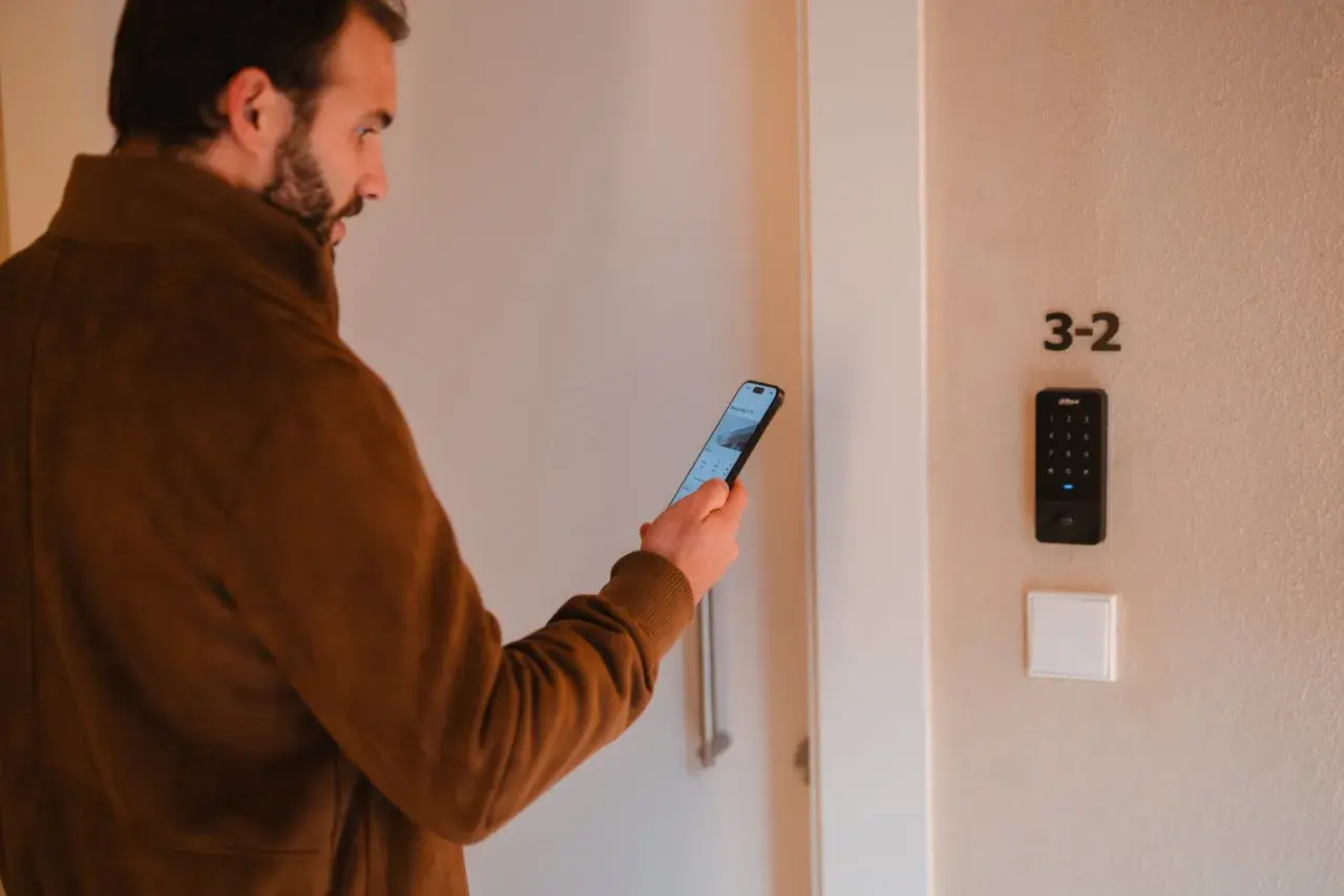 Hombre con móvil frente a puerta con teclado numérico. Una de las desventajas de la domótica es la dependencia tecnológica.