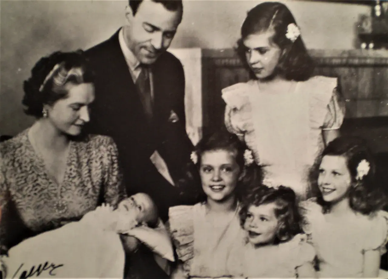 Familjefoto med prinsessan Sibylla och hennes barn. Bilden visar en familj med föräldrar och flera barn, inklusive en bebis. Prinsessan Sibylla bar en mönstrad klänning.