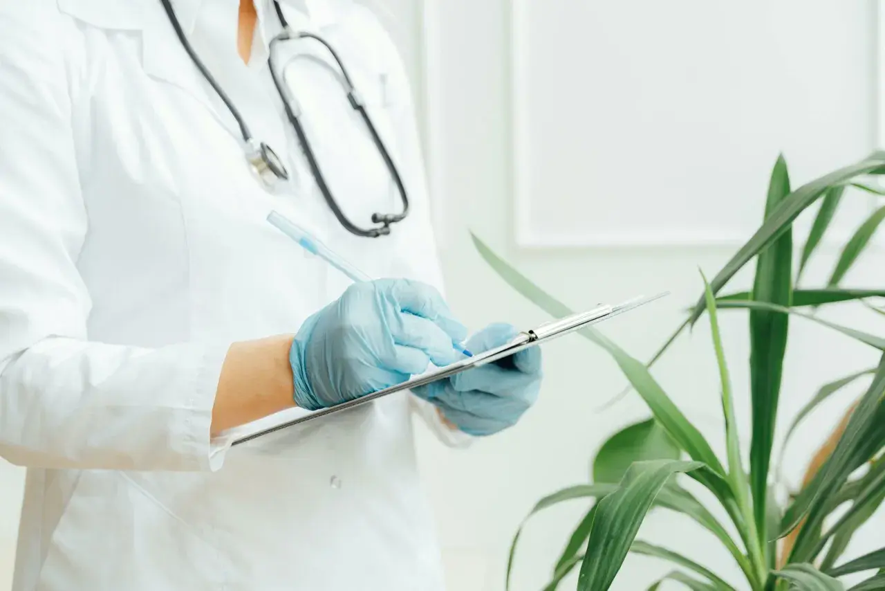 Medico con camice bianco e guanti blu scrive su un blocco appunti. Lo stetoscopio è appeso al collo. Il significato di "extramoenia" è legato a ciò che è fuori dalle mura, come un consulto medico fuori dall'ospedale.