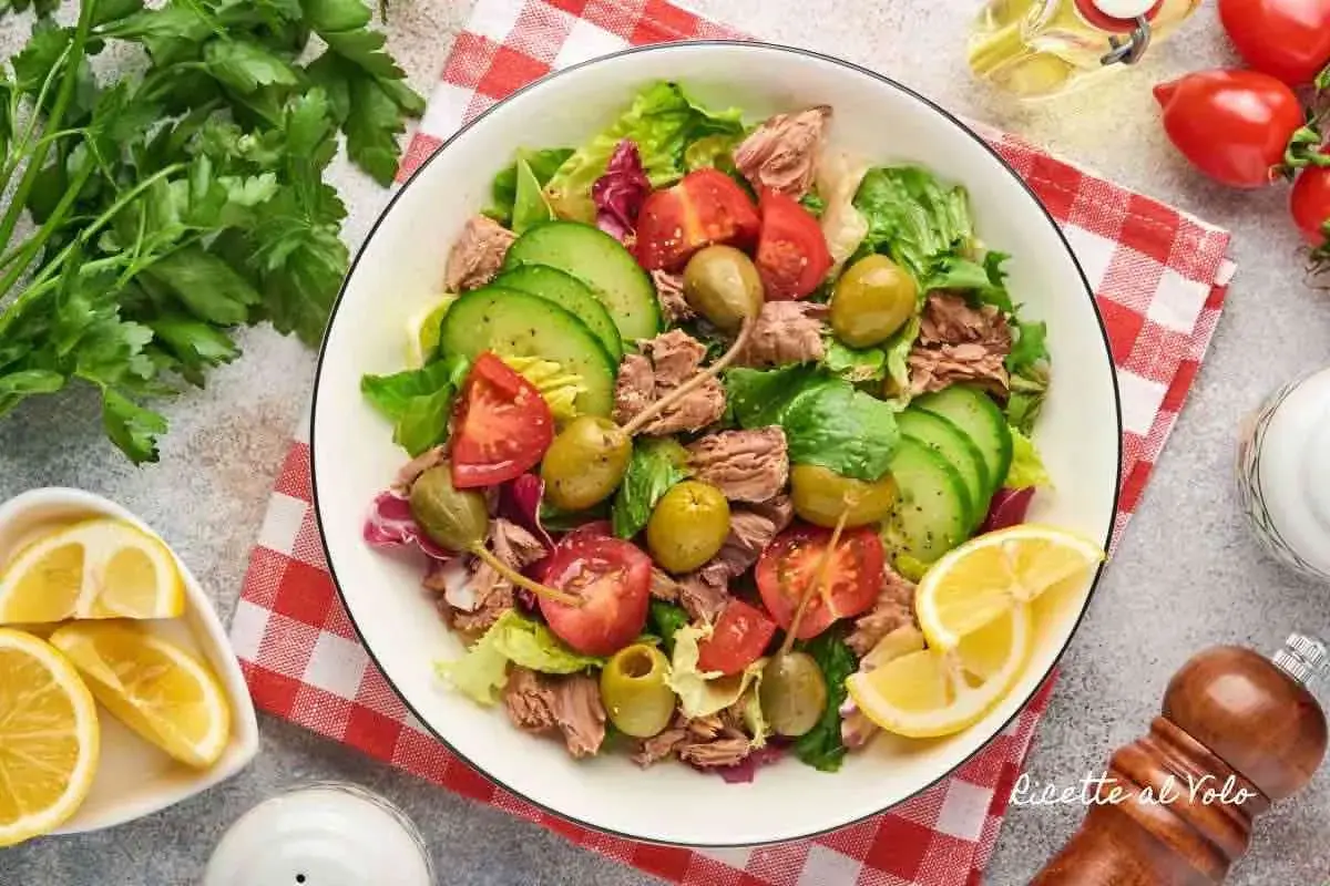 Insalata di tonno fresca e colorata con pomodori, cetrioli, olive e capperi, guarnita con limone.