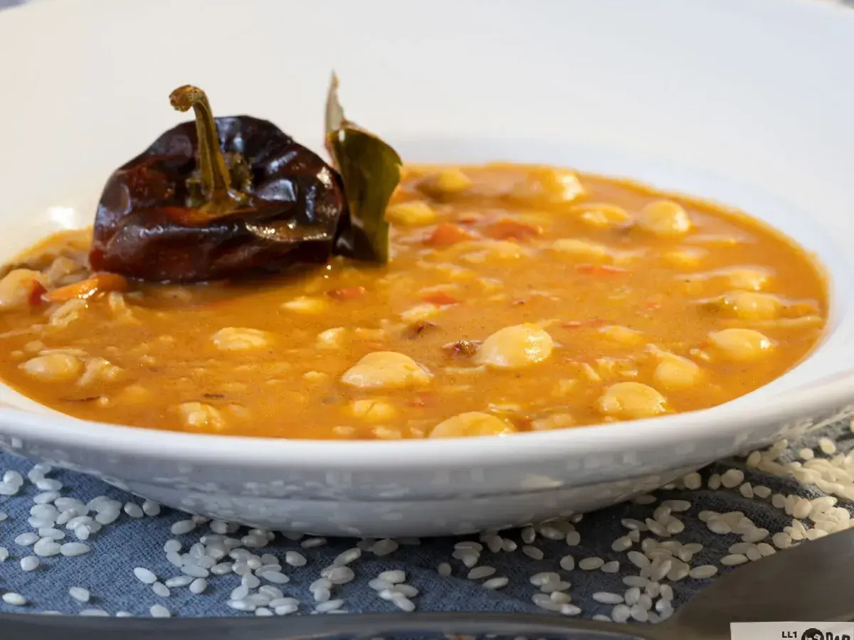 Un plato de garbanzos con arroz, con un pimiento seco y una hoja de laurel encima.