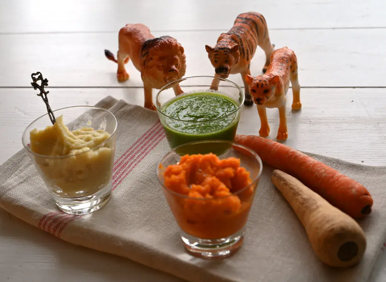 Lekfulla lejon och tigrar vakar över tre skålar med puréer – perfekt för plockmat bebis recept. Morötter och en grön puré ser aptitliga ut.
