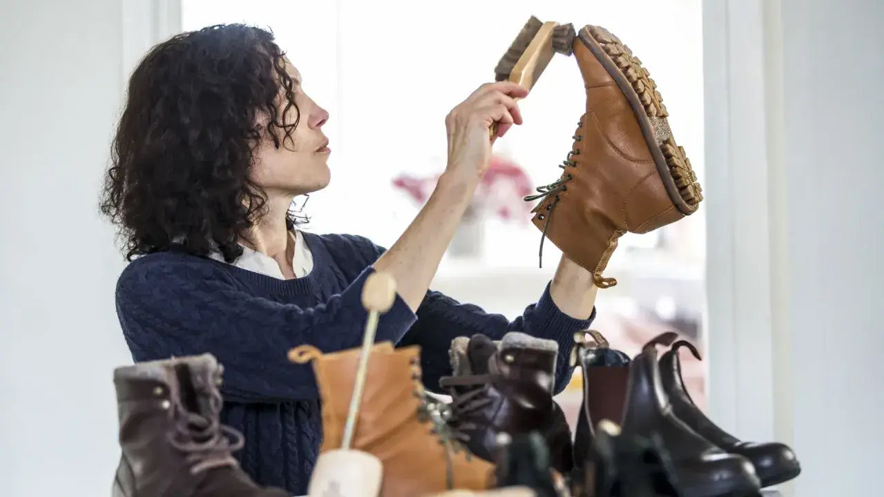 Une femme aux cheveux bouclés brosse une botte en cuir. Elle s'assure de la bonne fréquence de cirage de ses chaussures pour les garder en parfait état.