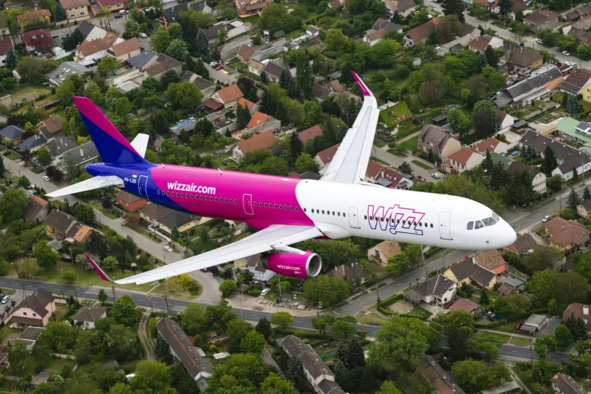 Różowy samolot Wizzair przelatuje nad osiedlem domów jednorodzinnych.