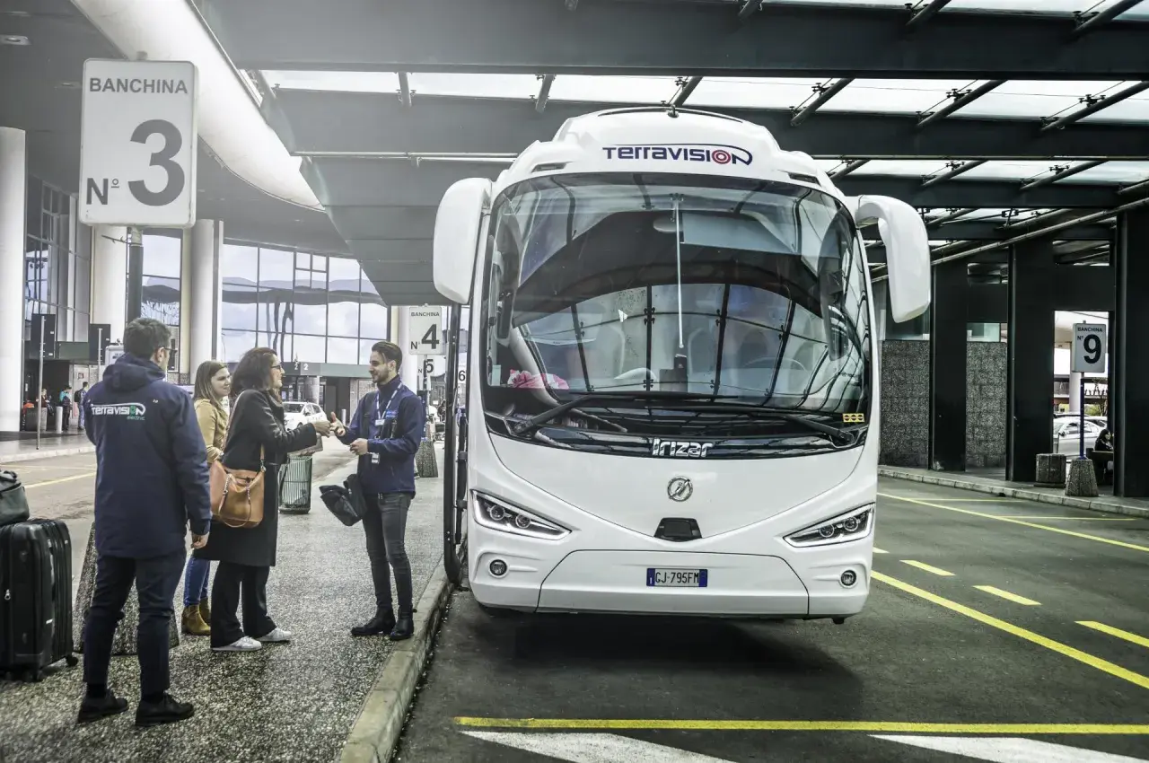 Autobus Terravision czeka na pasażerów na jednym z mediolan lotniska. Ludzie z bagażami rozmawiają z pracownikiem.