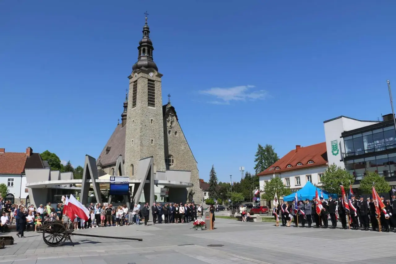 Uroczystość przed kościołem w Limanowej. Ludzie, delegacje w mundurach i polskie flagi.