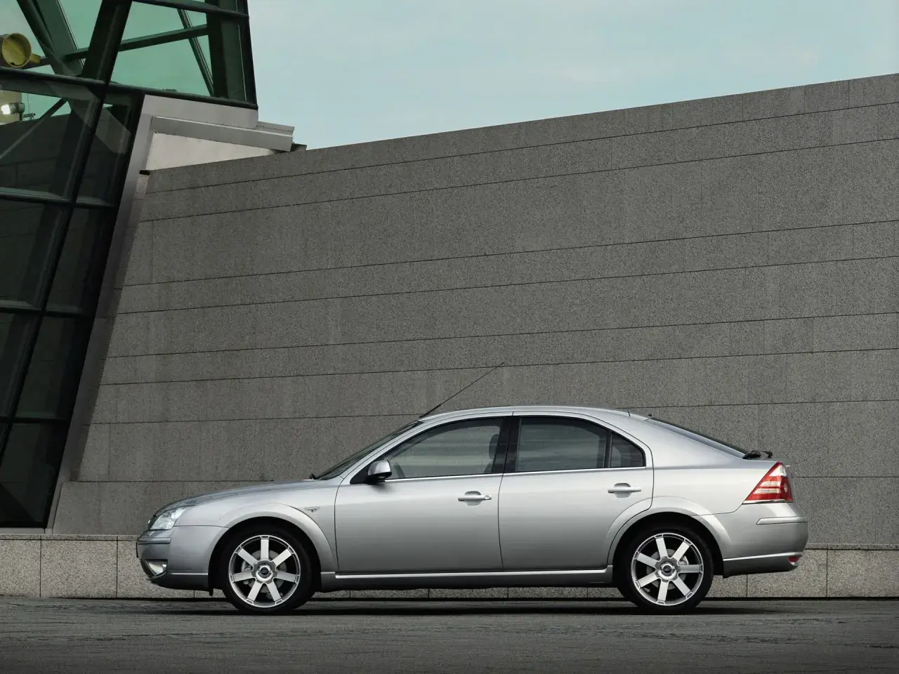 Srebrny Ford Mondeo MK3 2.0 TDCI stoi na tle nowoczesnego budynku z kamienną fasadą.