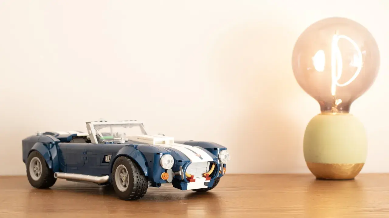 Ein blauer Lego Shelby Cobra steht neben einer leuchtenden Glühbirne.