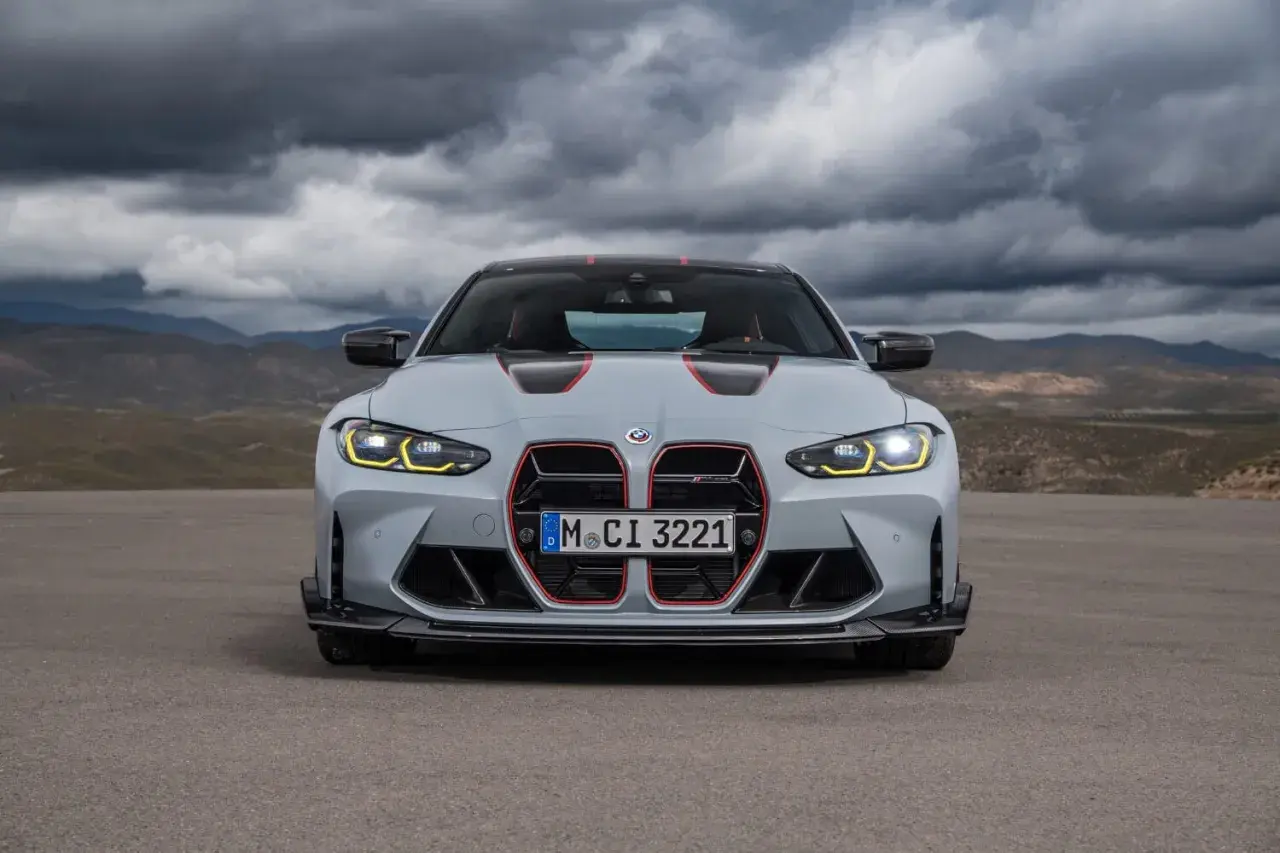 Szare BMW M4 CS z czerwonymi akcentami i agresywnym grillem, gotowe do jazdy po pustynnej drodze pod burzowym niebem.