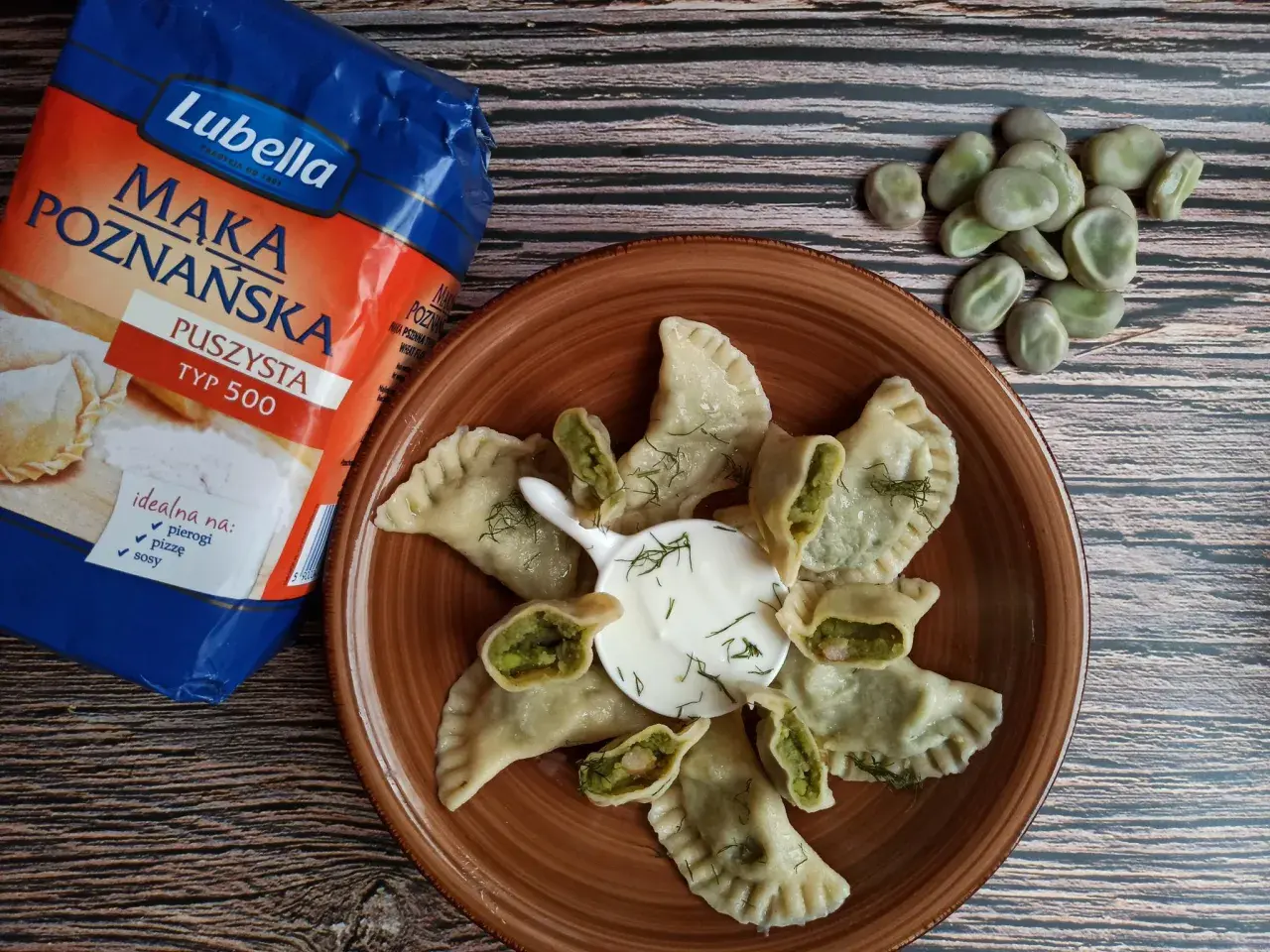 Pyszne pierogi z bobem, podane z kwaśną śmietaną i koperkiem, obok mąki Lubella.