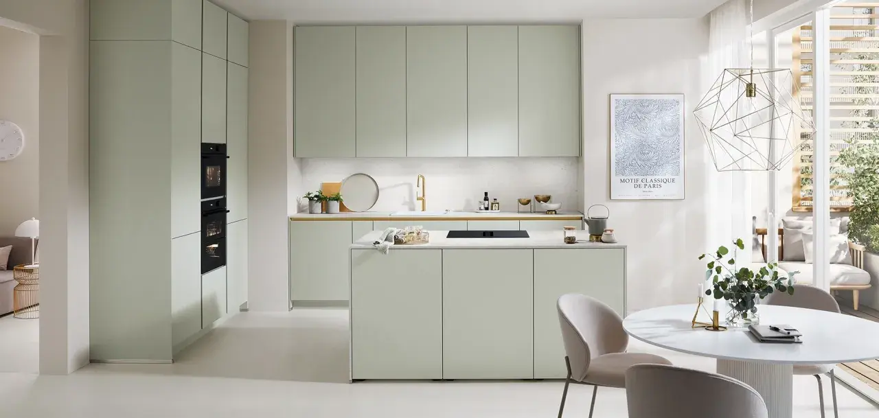 Moderna cocina verde con isla central, electrodomésticos integrados y una mesa redonda con sillas.