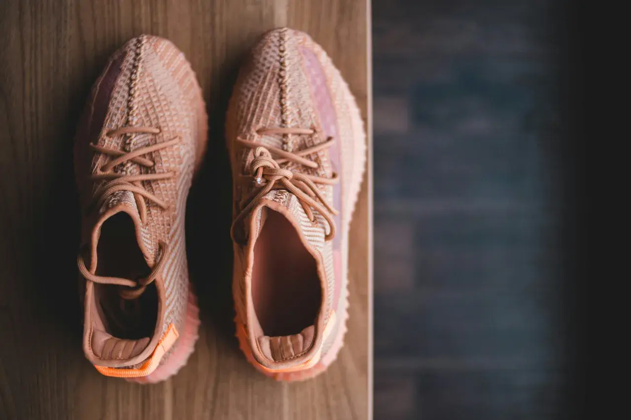 Pomarańczowe sneakersy z plecionki, idealne na szeroką stopę, leżą na drewnianym blacie.