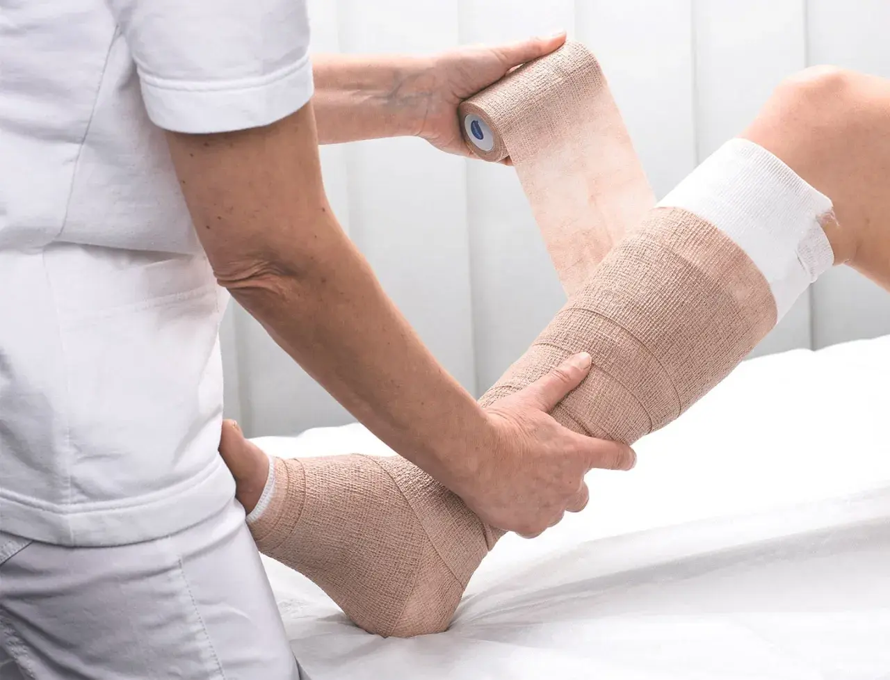 Eine Person wickelt einen Verband um ein Bein zur Kompression.